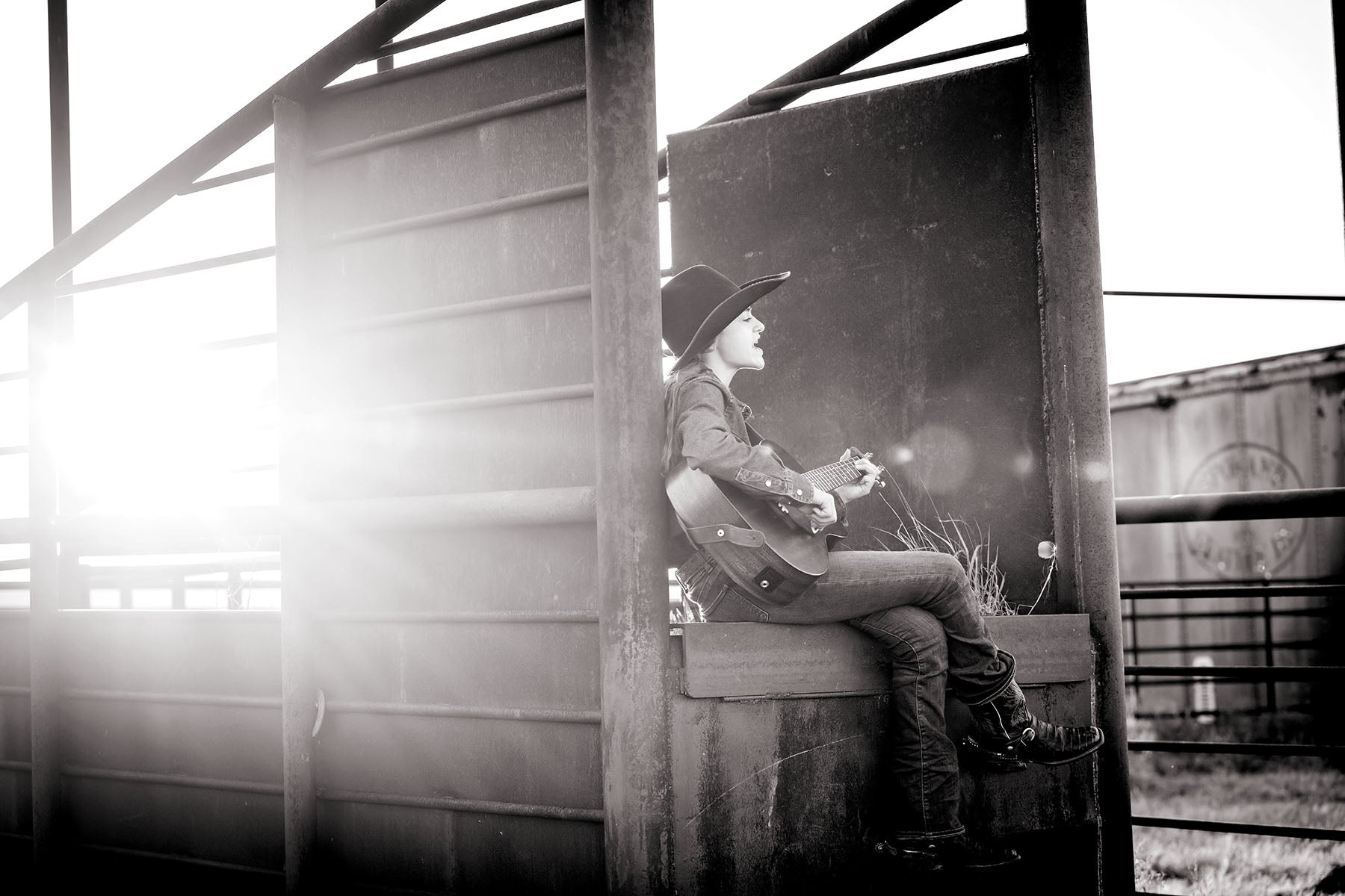 Selah Trinity Smith wearing a cowboy hat sitting on a cattle chute on the STS Ranch near Tell, Texas